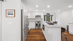 A modern kitchen with white cabinetry, stainless steel appliances, and a wooden floor. - Hayden Lake Home w/ Studio Suite & 2 Living Areas (Hayden Lake)