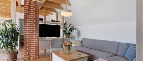 Un salon moderne avec un plafond en bois, un mur en briques, un téléviseur à écran plat, un canapé, une table basse et une plante en pot.