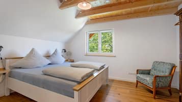 A bedroom with a wooden ceiling, a bed with pillows, a chair, and a window with a view of trees.