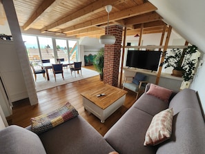 Ein modernes Wohnzimmer mit Holzboden, einem Fernseher, einem Sofa und einem Essbereich mit Stühlen und einem Tisch.