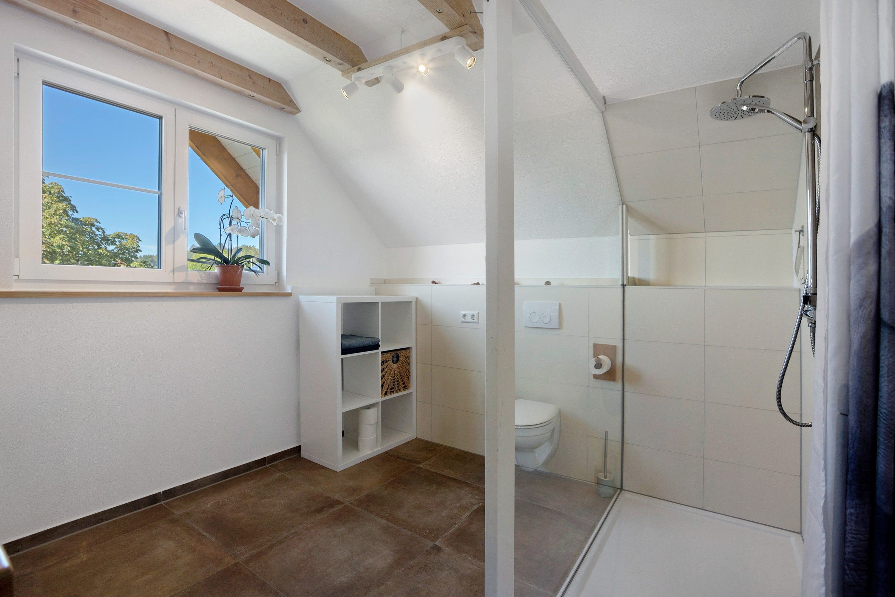 Ein Badezimmer mit Dusche, Toilette und einem Fenster mit Pflanze.