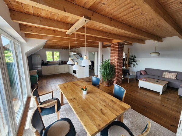 Ein großzügiger Wohnbereich mit einem Holzessttisch, Stühlen, einer Couch und einer Küche im Hintergrund.