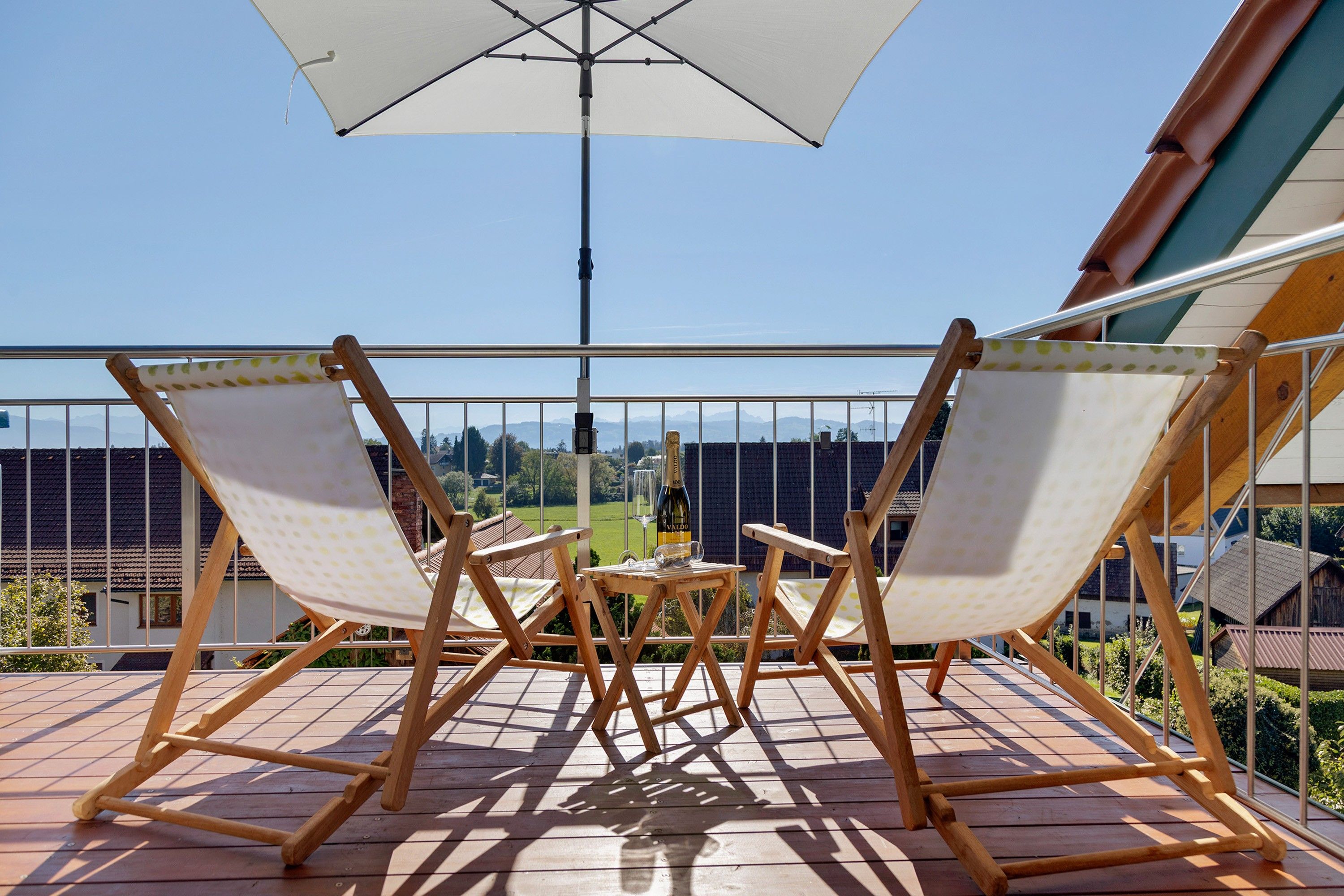A wooden deck with two folding chairs and a table, an umbrella, and a view of a cityscape.