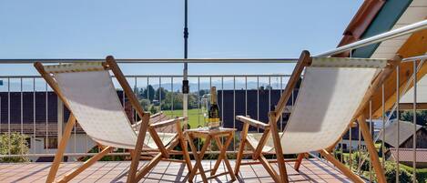 A wooden deck with two folding chairs and a table, an umbrella, and a view of a cityscape.