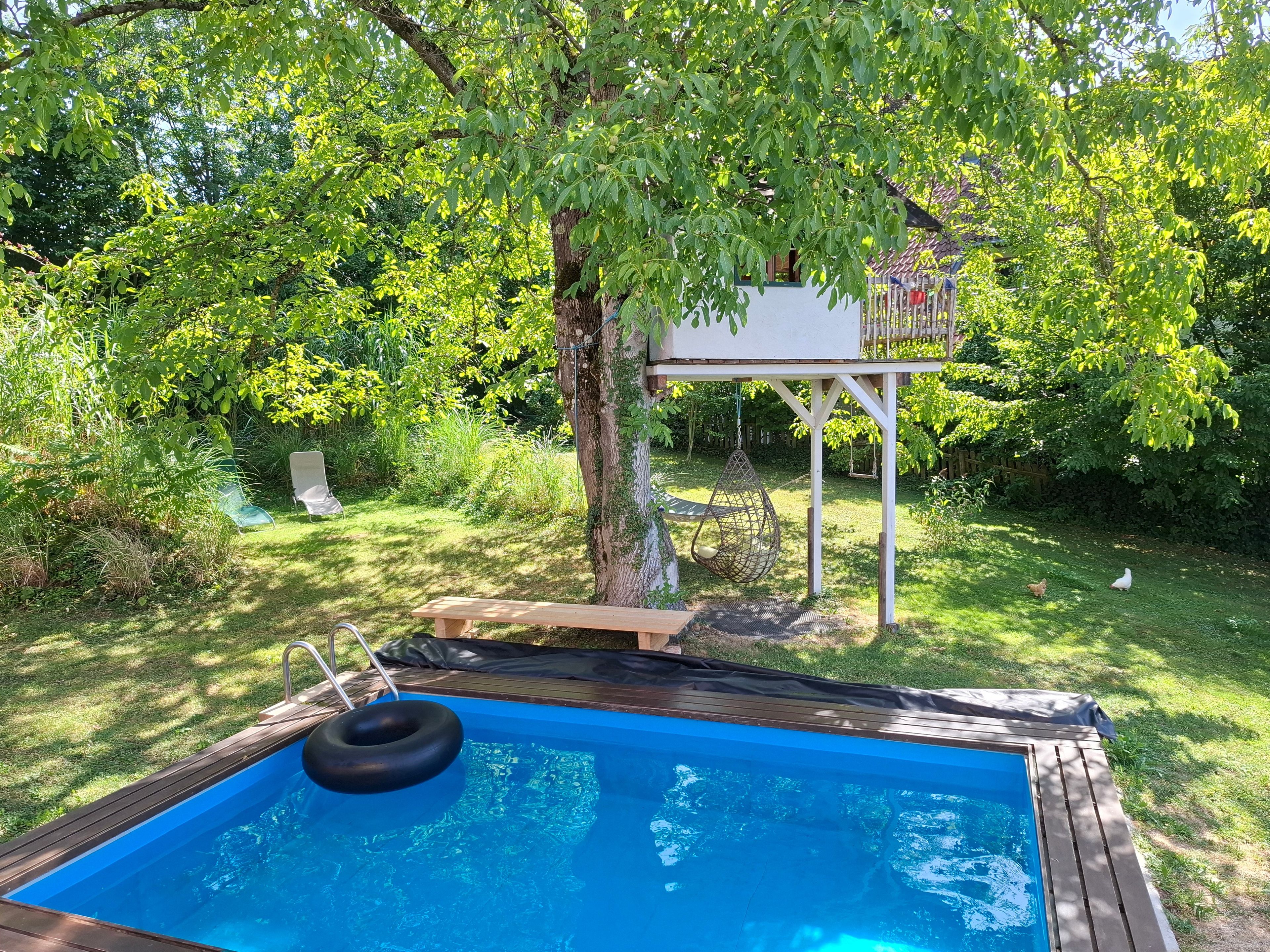 Ein Garten mit einer Holzterrasse, einem kleinen Pool und einem Hängesessel.