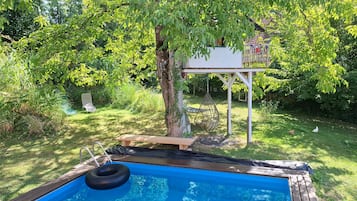 Ein Garten mit einer Holzterrasse, einem kleinen Pool und einem Hängesessel.