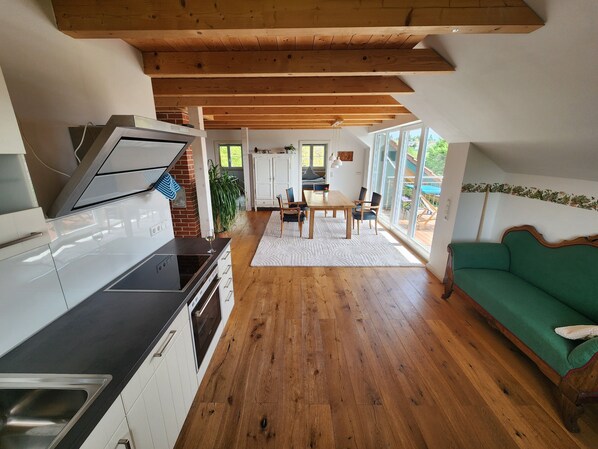 A modern kitchen with a dining area, wooden floors, and a green sofa. - Jacklis House anno 1657 – Eco Apartment with Mountain Views, Large Garden & Pool (Bodolz)