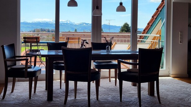 A dining area with a table and chairs, large windows with a mountain view, and pendant lights. - Jacklis House anno 1657 – Eco Apartment with Mountain View, Large Garden & Pool (Bodolz)