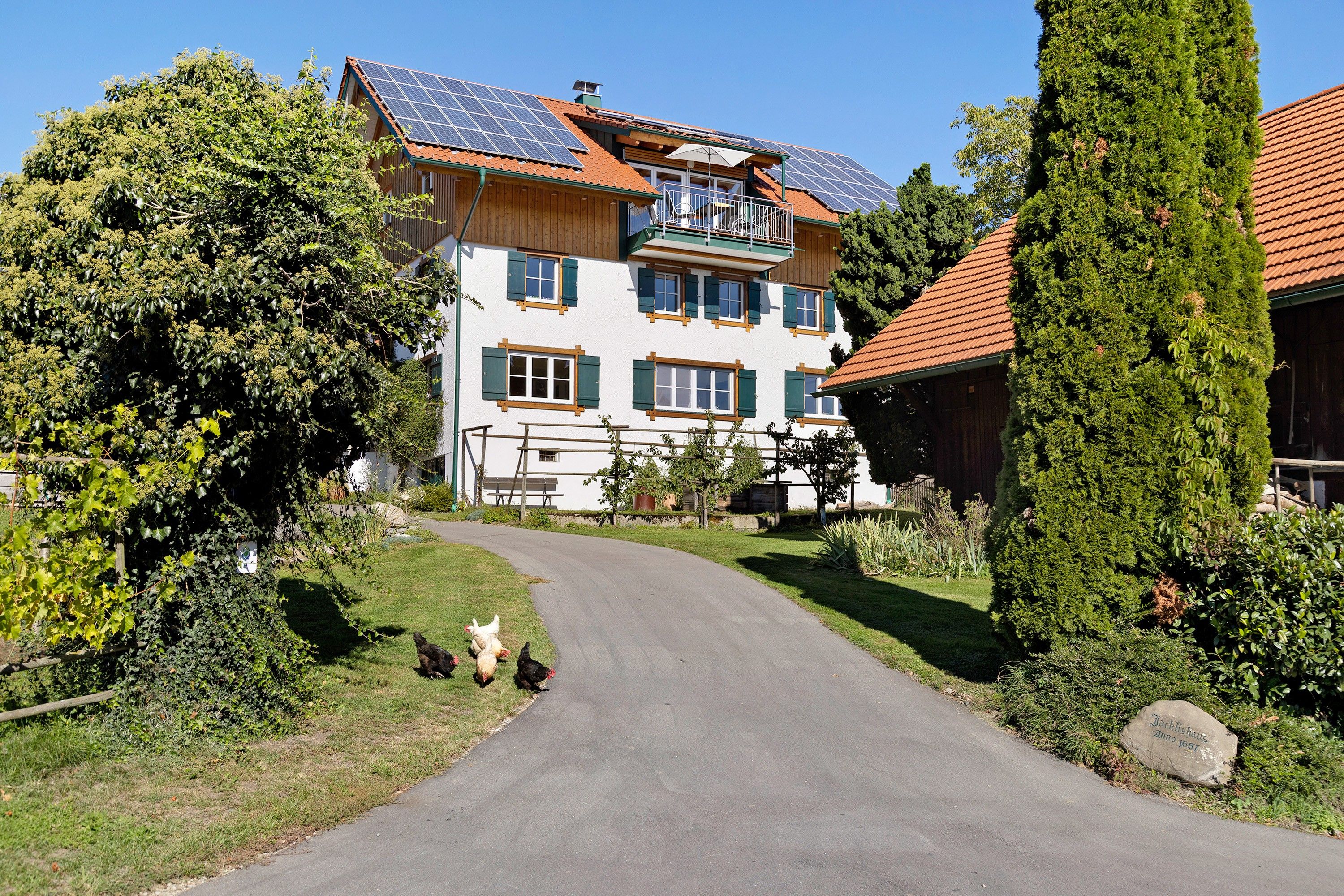 A two-story house with a sloped roof, solar panels, and a garden with chickens.