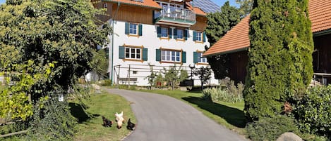 A two-story house with a sloped roof, solar panels, and a garden with chickens.