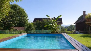 A rectangular swimming pool with a wooden deck, surrounded by grass and trees, with a house in the background. - Jacklis House anno 1657 – Eco Apartment with Mountain View, Large Garden & Pool (Bodolz)