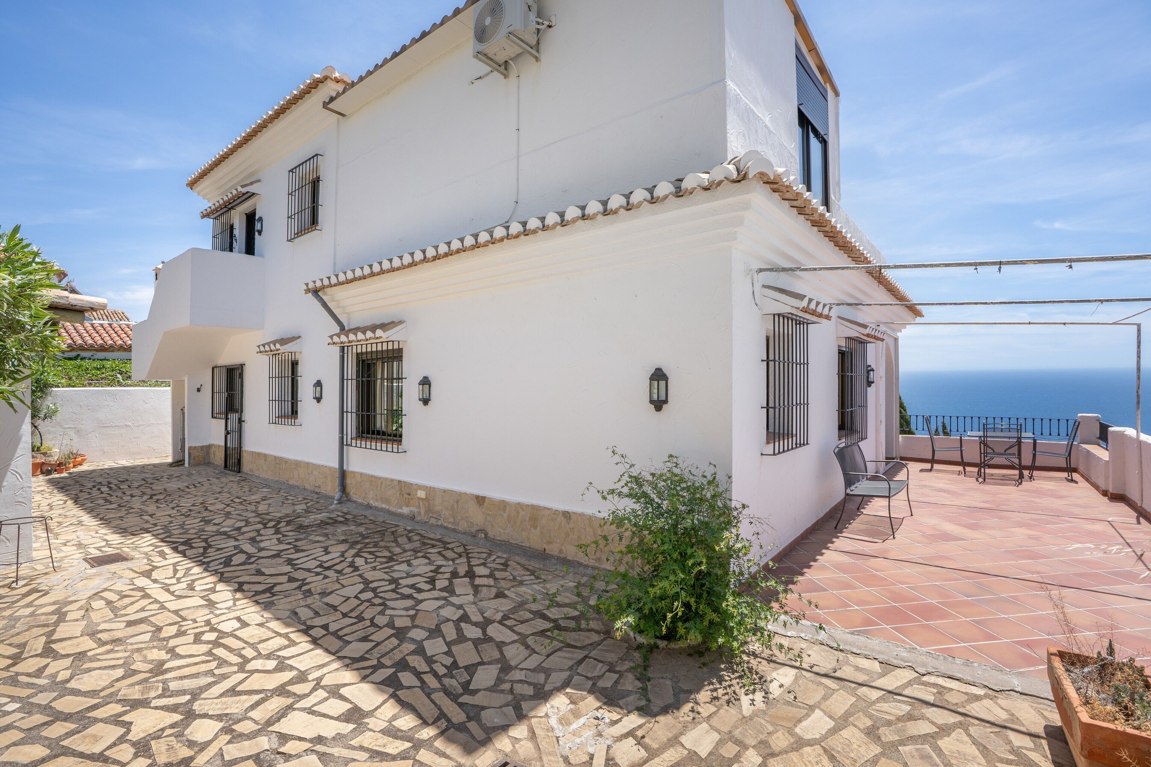 A two-story building with a tiled patio, a small garden, and a view of the sea.