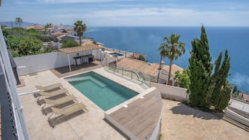 Ein Pool auf dem Dach mit Liegestühlen, einem kleinen Tisch und Blick aufs Meer.