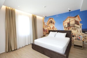 Una habitación de hotel con una cama grande, cortinas color beige, un mural de edificios y suelo de madera.