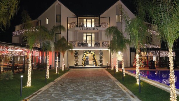 A two-story villa with a pool, surrounded by palm trees and decorated with lights. - Vila Lira (Durres)