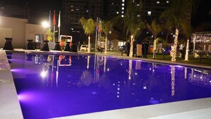 A swimming pool with a clear blue water surface, surrounded by palm trees and illuminated by string lights. - Vila Lira (Durres)