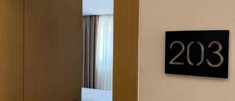 Una habitación de hotel con una puerta de madera, un cartel con el número '203' en la pared, una cama y una mesita de noche.