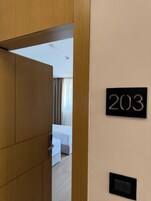 Ett hotellrum med en dörr av trä, ett nummerskylt med siffran ’203’ på väggen, en säng och ett sängbord.