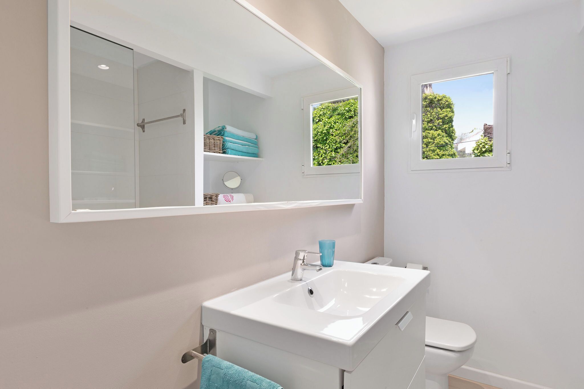 Un baño con lavabo blanco, espejo, ventana y ducha.