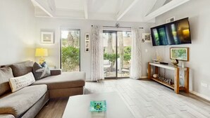 A living room with a sofa, a coffee table, a TV mounted on the wall, and a sliding glass door leading to an outdoor area. - Palmetto Dunes Beach Villa | Golf, Pool,  Dogs OK (Hilton Head Island)