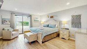 A bedroom with a bed, a chair, a nightstand, and a wall-mounted macrame. - Palmetto Dunes Beach Villa | Golf, Pool,  Dogs OK (Hilton Head Island)