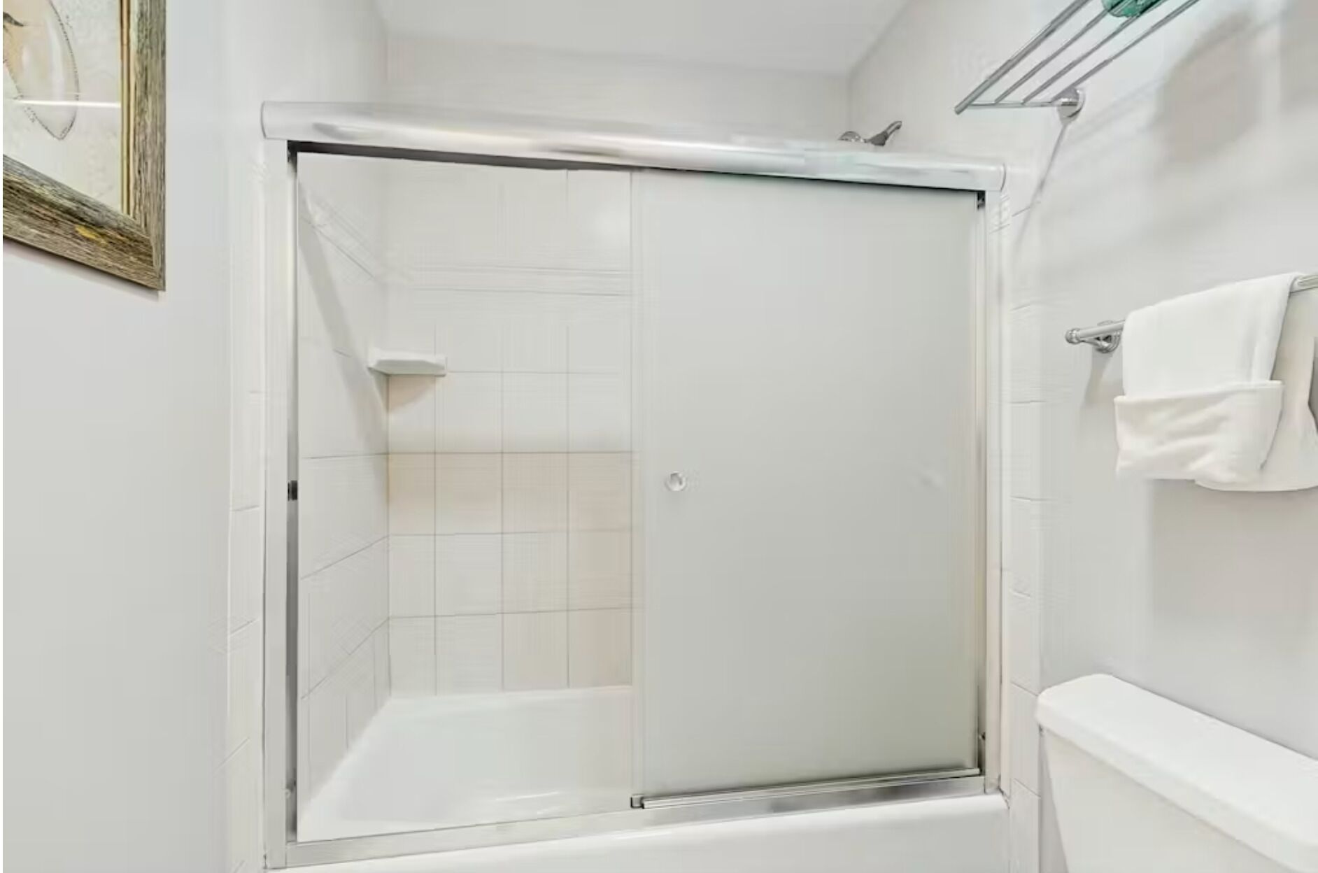 Une douche avec une porte en verre, des murs recouverts de carreaux blancs et un porte-serviettes.