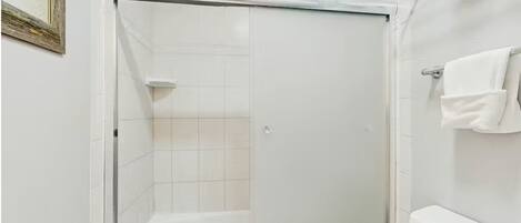 Une douche avec une porte en verre, des murs recouverts de carreaux blancs et un porte-serviettes.