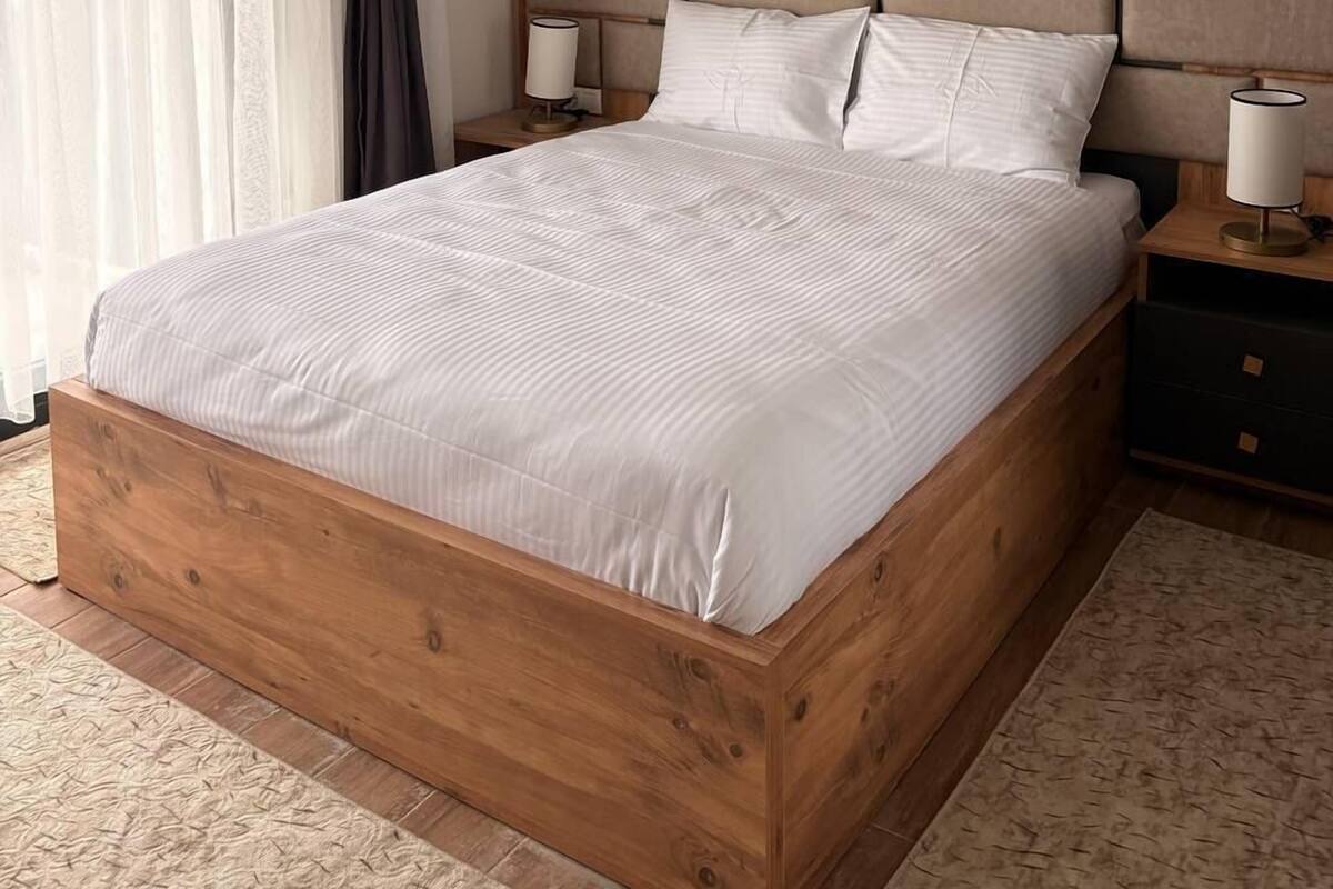 Een slaapkamer met een houten bed, twee nachtkastjes, een hoofdbord en een raam met gordijnen.