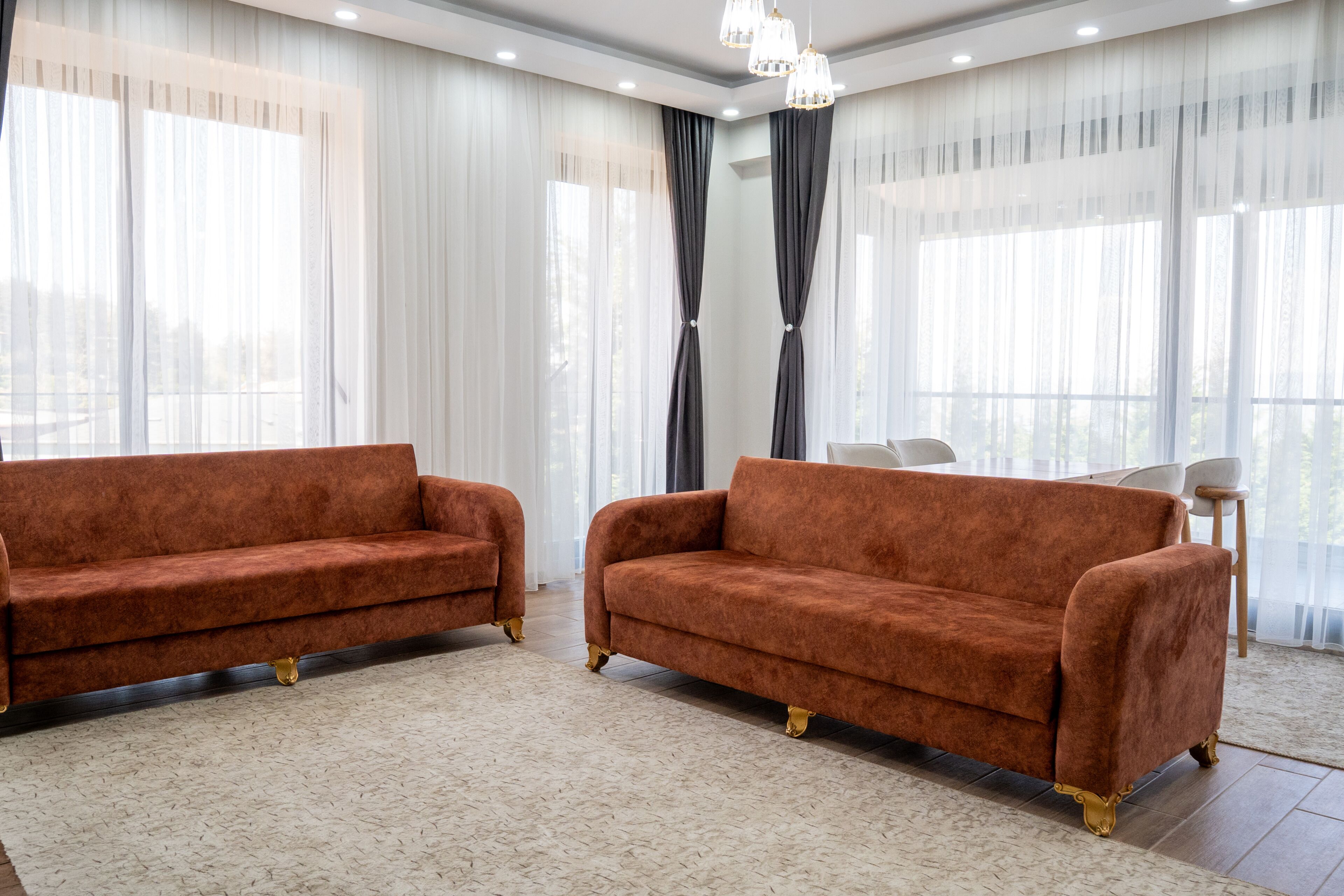 Una habitación con dos sofás, un candelabro y ventanas amplias con cortinas translúcidas.