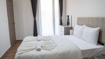 Una cama bien tendida con sábanas blancas, una mesita de noche con lámpara y una ventana con cortinas.