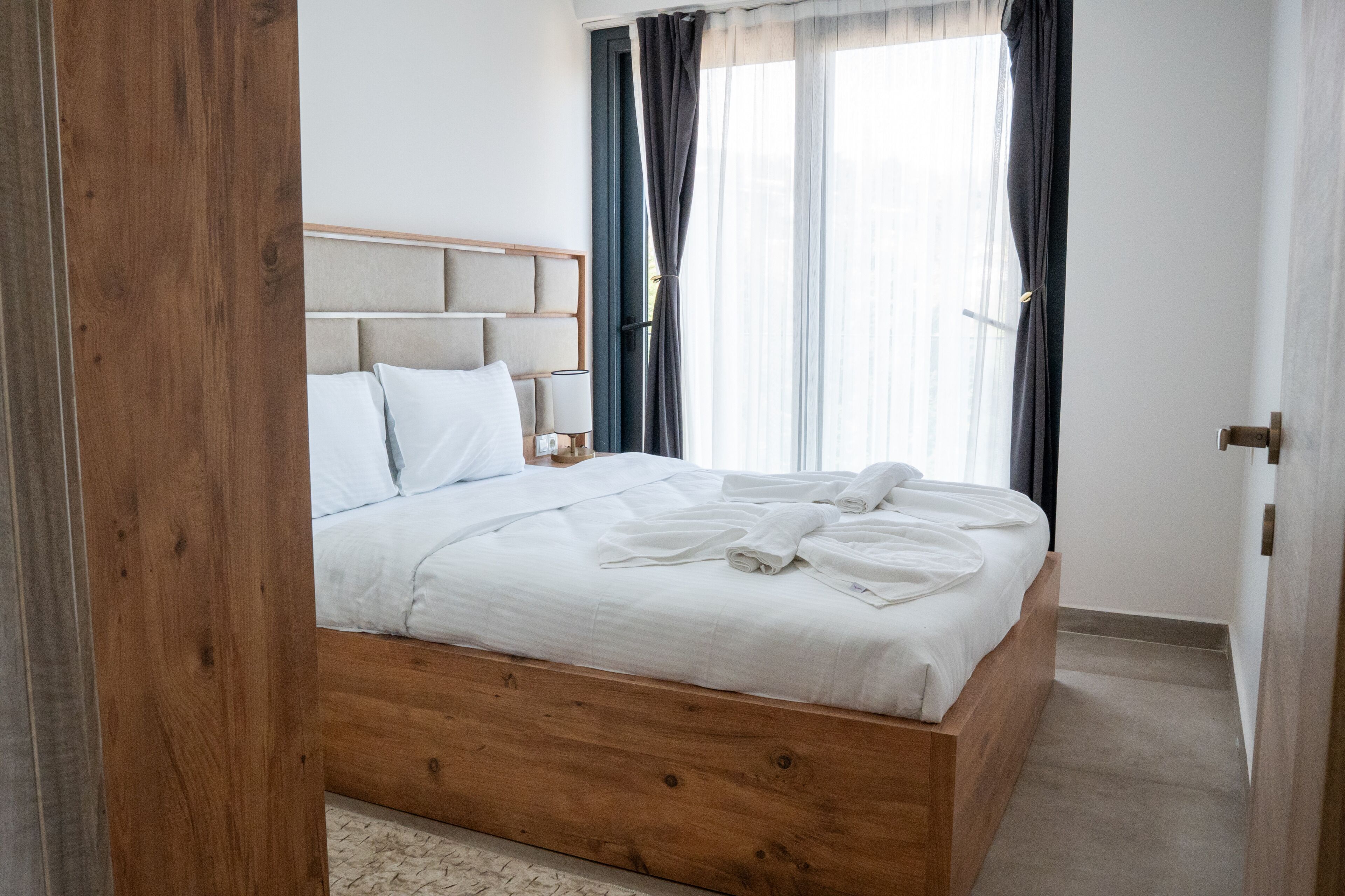 Un lit bien fait, avec du linge de lit blanc, une tête de lit en bois et une table de chevet avec une lampe.