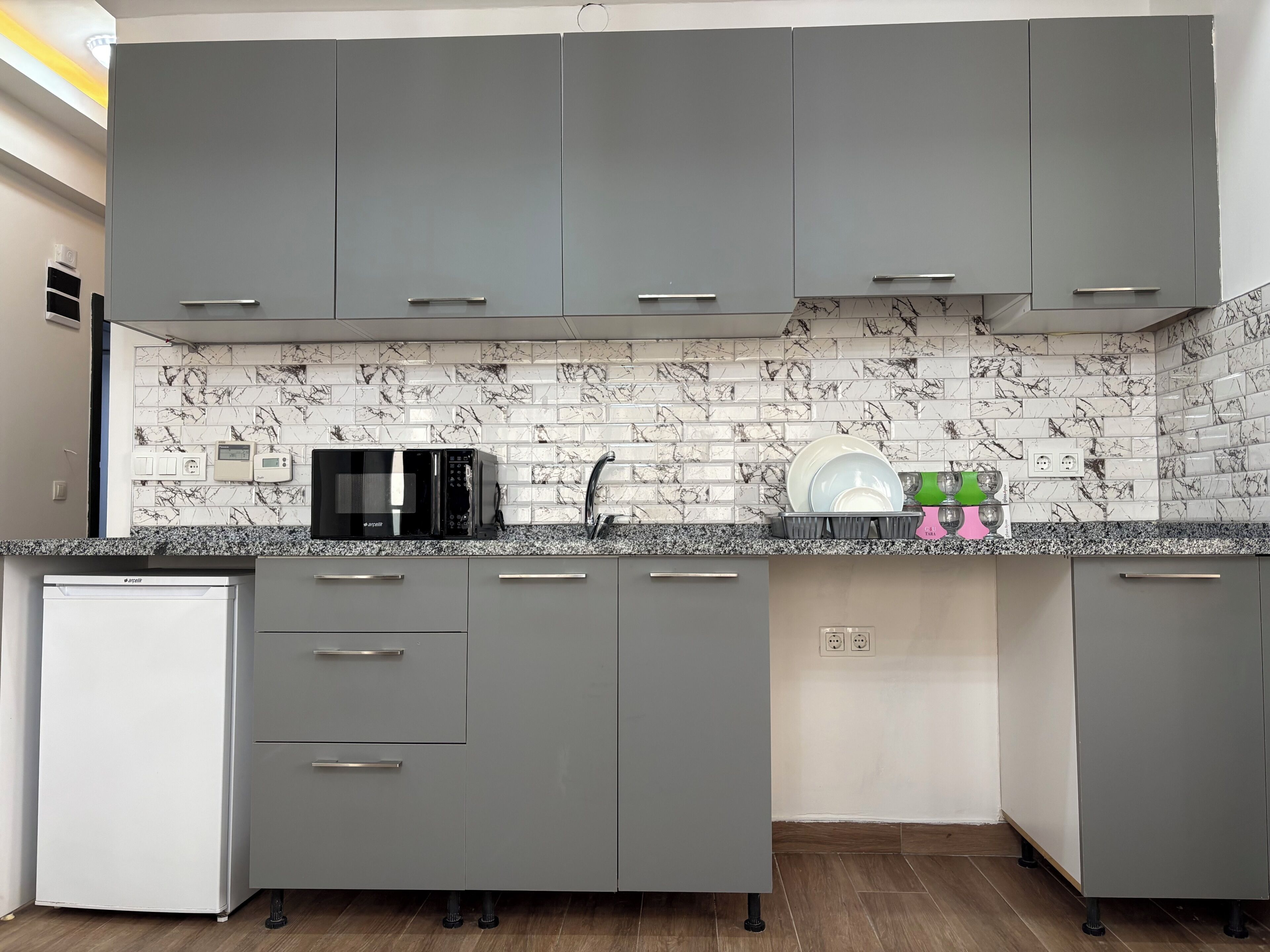 Una cucina moderna con mobili grigi, un forno a microonde, un lavello e un espositore per piatti.