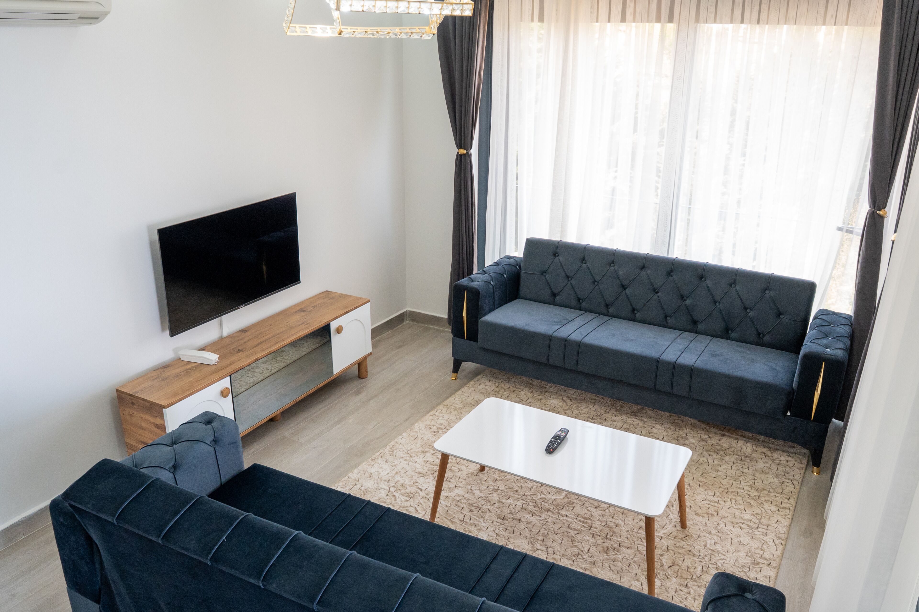 A modern living room with a flat-screen TV, a dark blue sofa, a white coffee table, and a wooden sideboard.