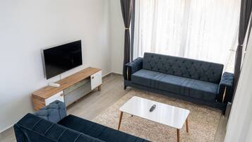 A modern living room with a flat-screen TV, a dark blue sofa, a white coffee table, and a wooden sideboard.