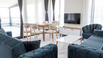 A modern living room with a sofa set, a dining table with chairs, a TV, and a balcony with curtains.