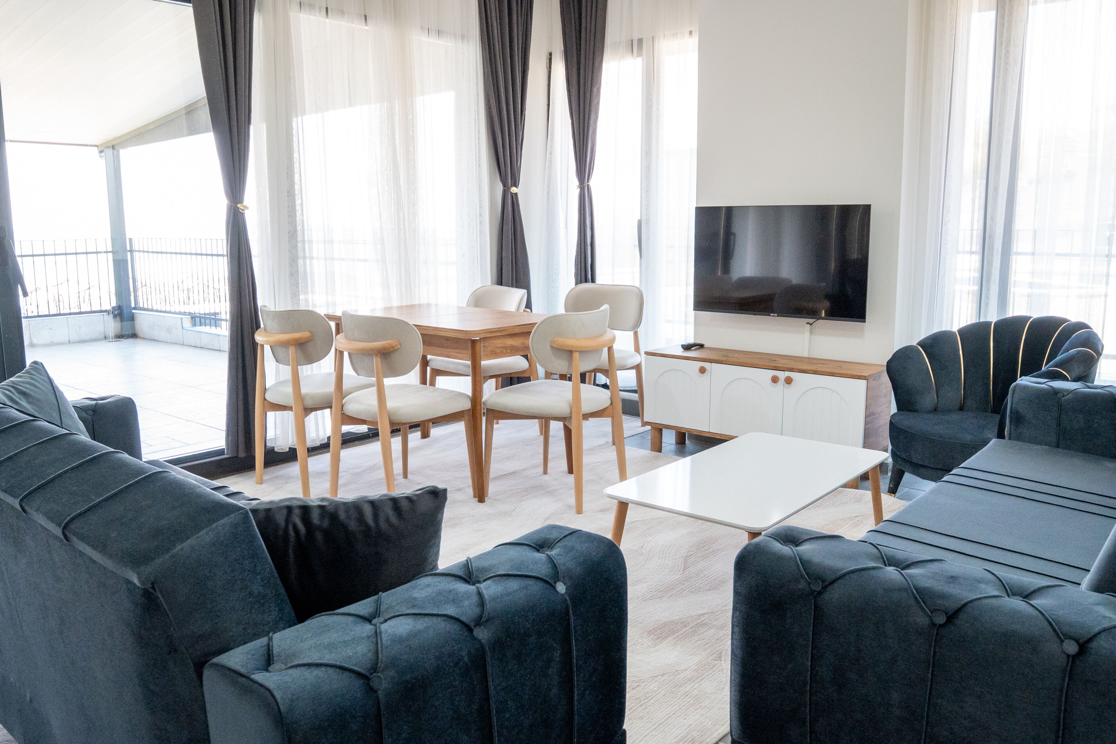 A modern living room with a sofa, chairs, a TV, and a balcony view.