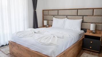 Ein hölzernes Bett mit Kopfteil, weiße Bettwäsche, zwei Nachttische mit Lampen und ein Schminktisch mit Schubladen.