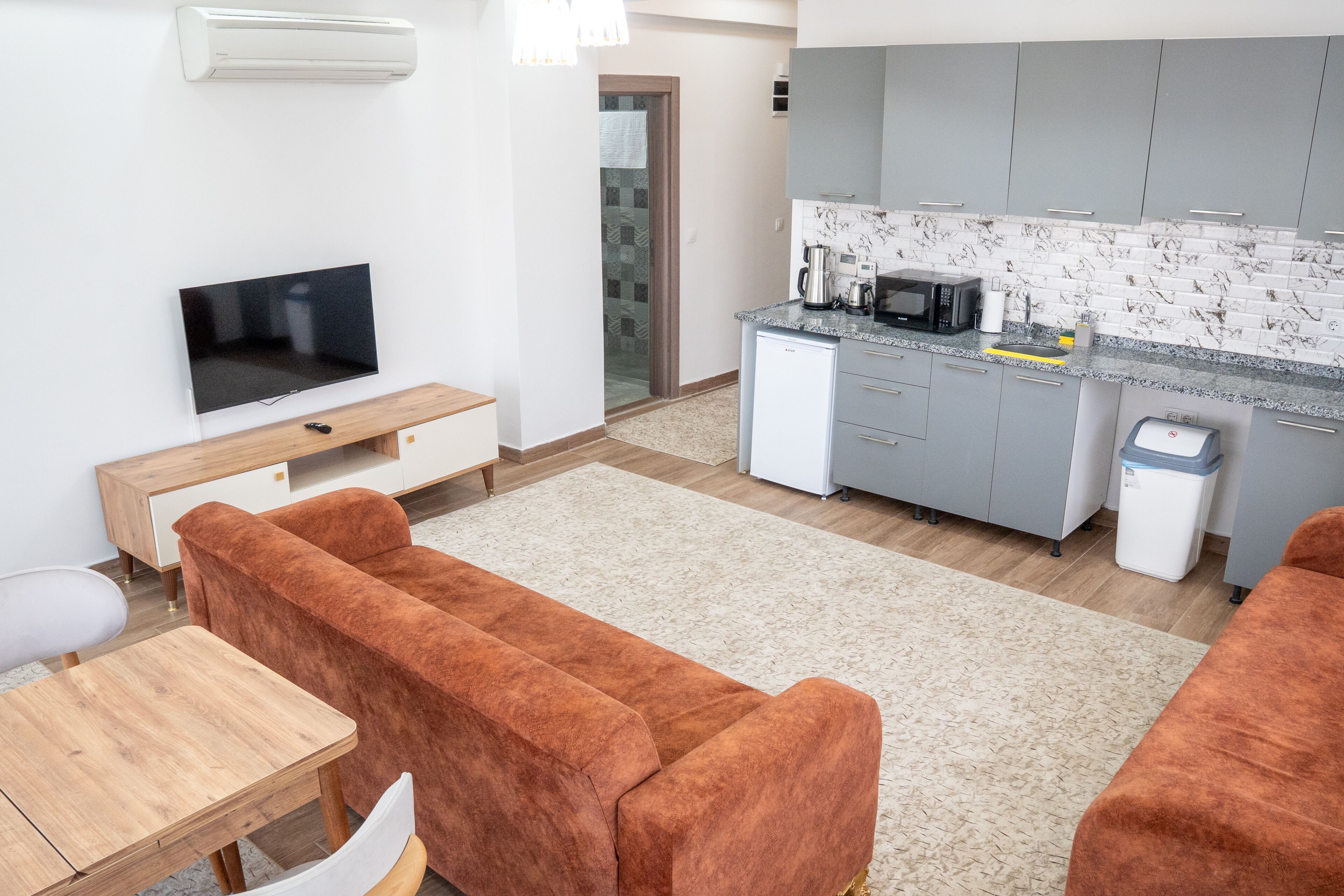 A modern living room with a sofa, TV, and a kitchen area with grey cabinets and a tiled backsplash.