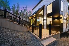 Uma casa moderna com deck de madeira, guarda-corpo preto e garagem.