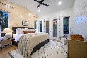 Quarto com cama, abajures, ventoinha no teto e vista do exterior através de grandes janelas.