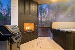 Um terraço com lareira a lenha, banheira de hidromassagem e vista para uma floresta.