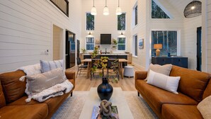 A spacious living area with a large sofa, a coffee table with a vase, and a dining area with a kitchen in the background. - Modern Chalet Retreat | 1BR + Loft & Bunks in Secluded Broken Bow (Broke Bow)