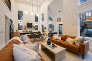 A spacious living room with a large sofa, a coffee table, and a dining area with a kitchen in the background. - Modern Chalet Retreat | 1BR + Loft & Bunks in Secluded Broken Bow (Broke Bow)