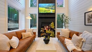 A living room with two brown sofas, a central coffee table, and a fireplace. - Modern Chalet Retreat | 1BR + Loft & Bunks in Secluded Broken Bow (Broke Bow)