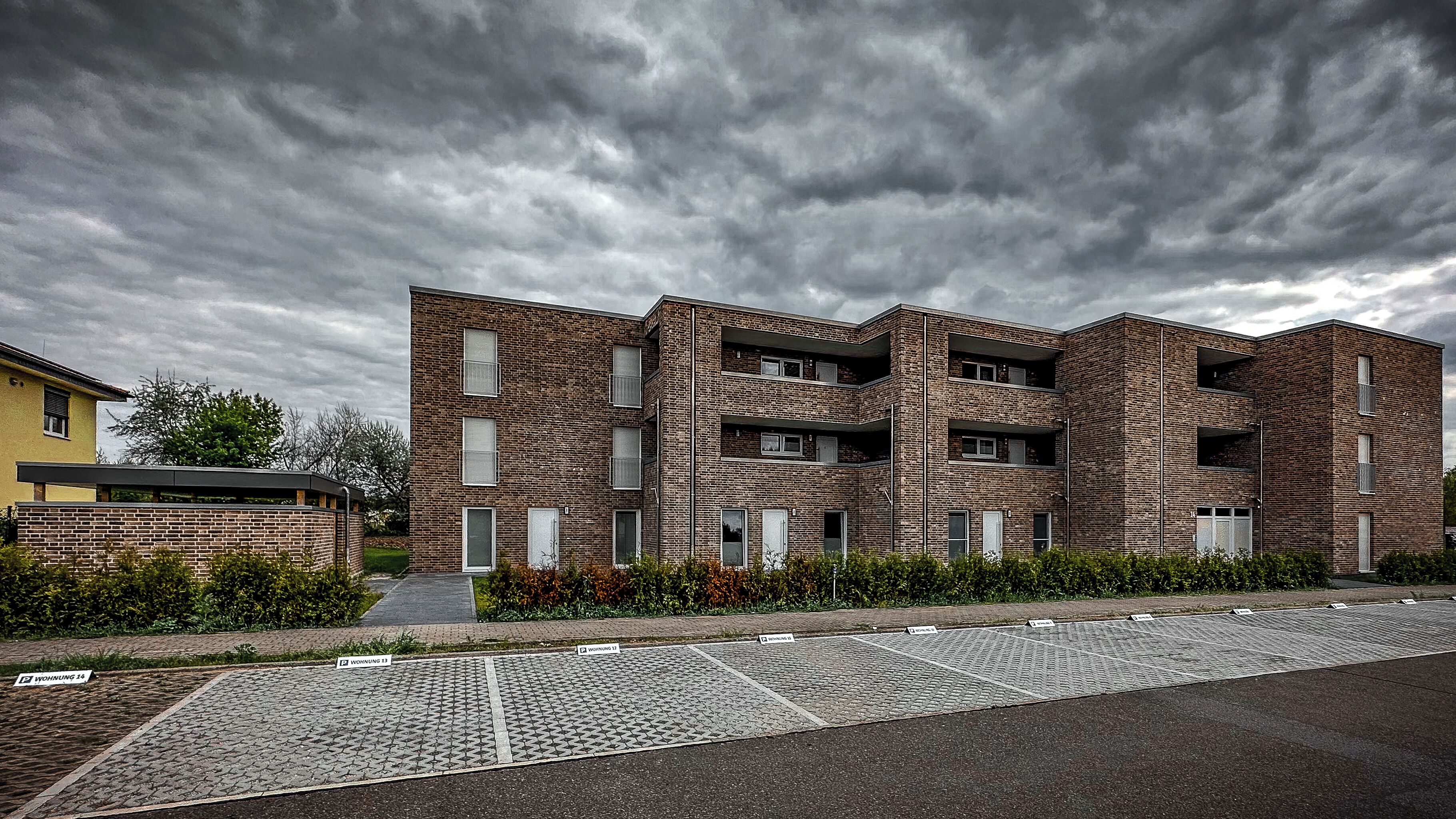 Un immeuble moderne à plusieurs étages, doté d’une façade en briques, de nombreux balcons et d’un espace d’entrée pavé.