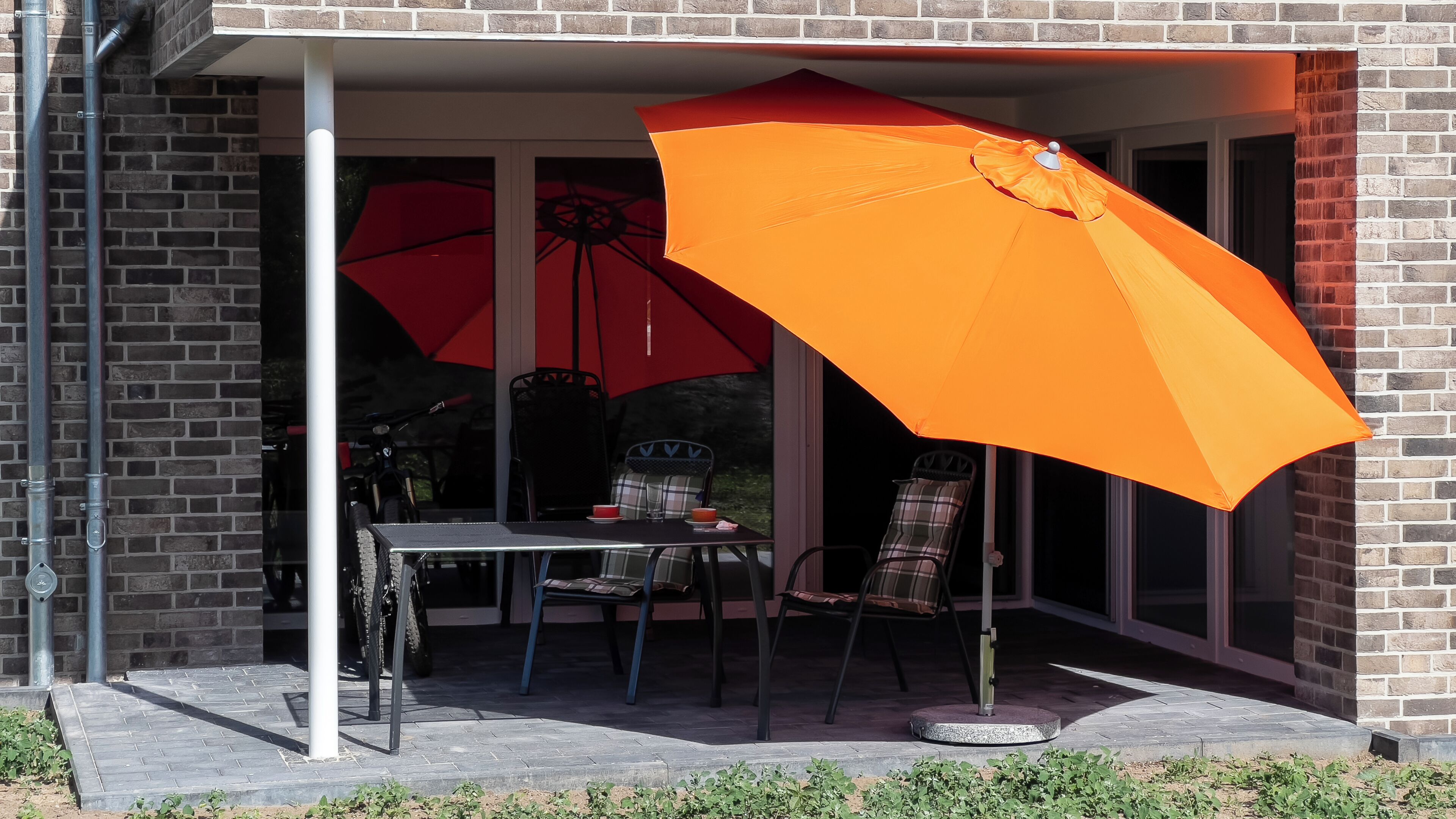 Une terrasse couverte avec une table et des chaises, deux parasols et un mur en briques.