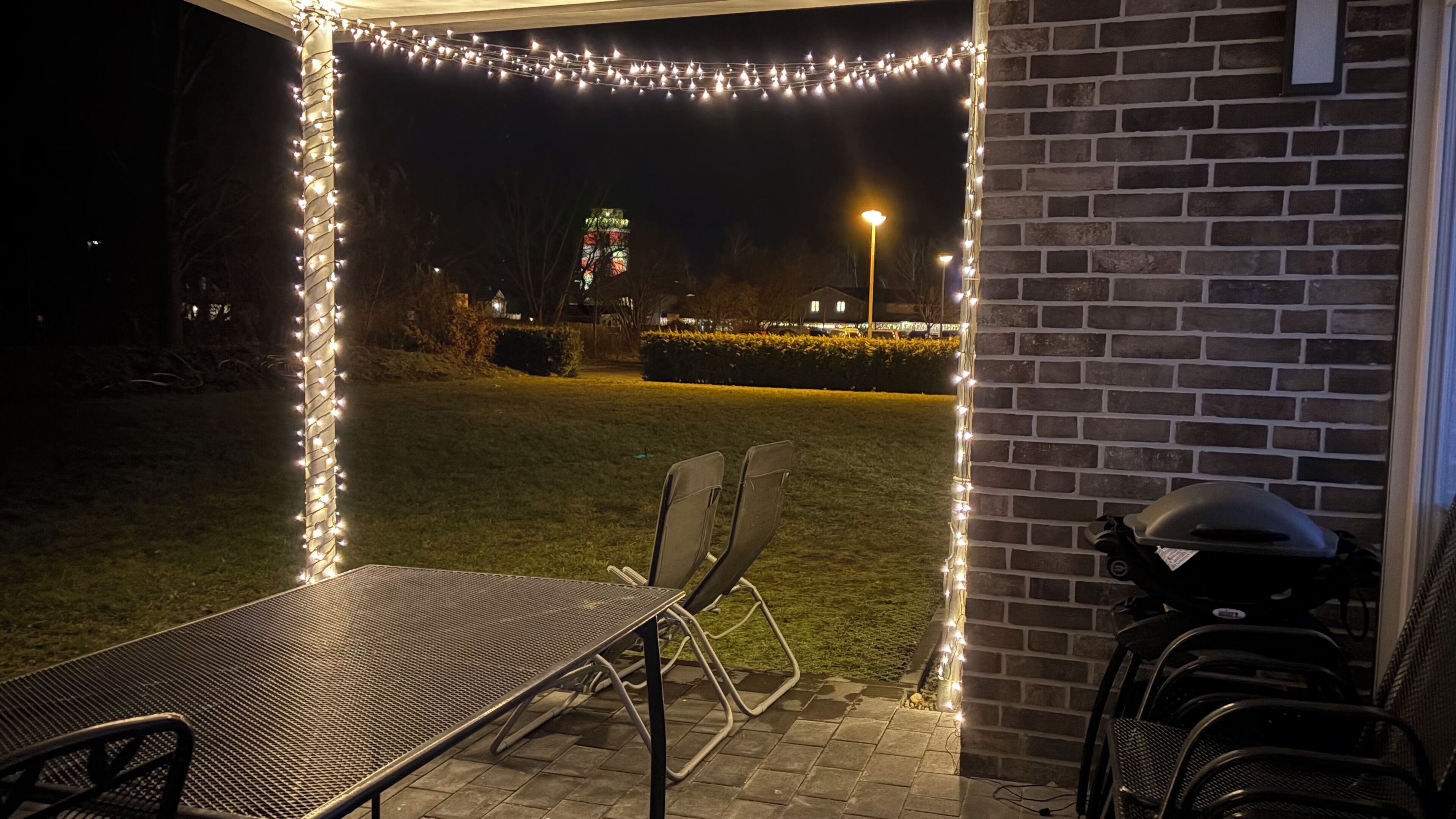 An outdoor patio area with a metal table and chairs, a brick wall, and string lights.