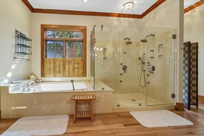 Een badkamer met een glazen douchecabine, een dubbele wastafel en een houten bankje.