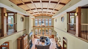 Un intérieur spacieux avec un haut plafond en bois, de grandes fenêtres, un coin salon avec un canapé et une table basse, et une vue sur la mer.