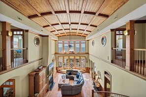 Un intérieur spacieux avec un haut plafond en bois, de grandes fenêtres, un coin salon avec un canapé et une table basse, et une vue sur la mer.